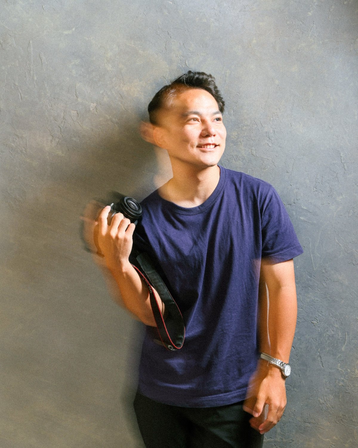 カメラを肩にかけて微笑む、フォトグラファー茂朋志のプロフィール写真